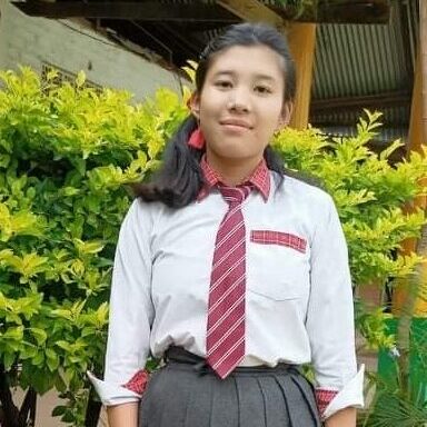 A girl in school uniform standing next to bushes.