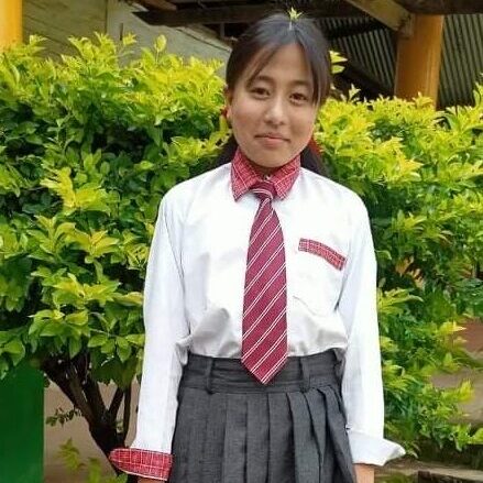A girl in school uniform standing next to bushes.