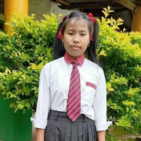 A girl in school uniform standing next to bushes.