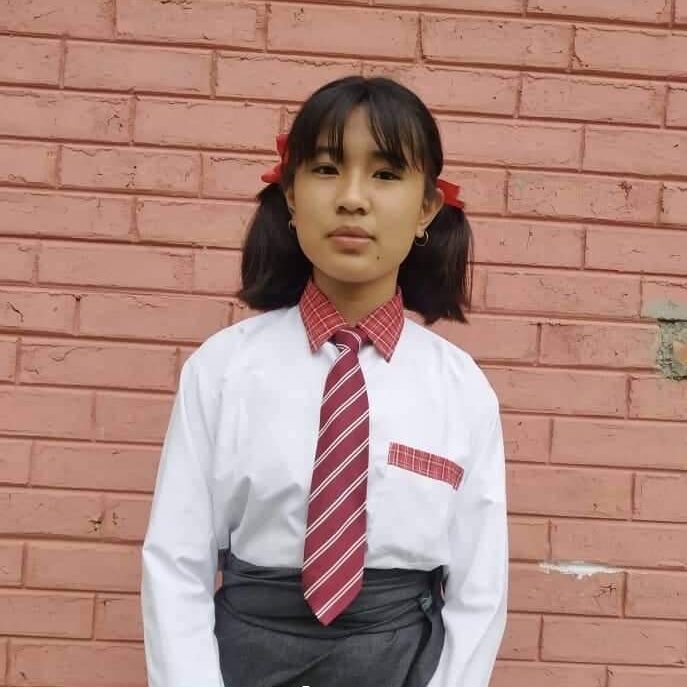 A girl in school uniform standing against a brick wall.