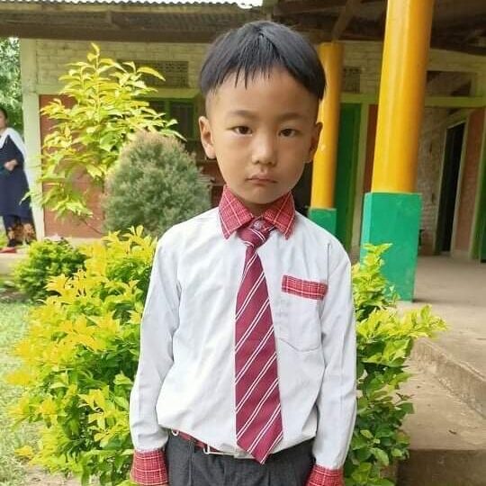 A young boy in a tie standing outside.