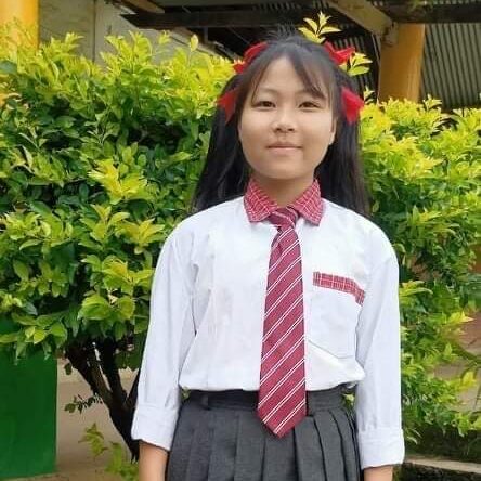 A girl in school uniform standing next to bushes.
