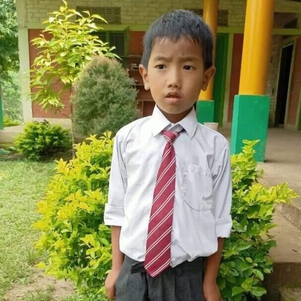 A young boy in a tie standing outside.