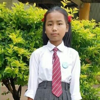 A girl in school uniform standing next to a bush.