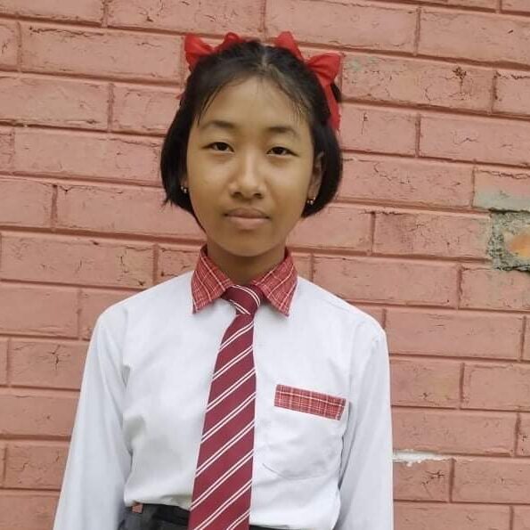 A girl in school uniform standing against a brick wall.