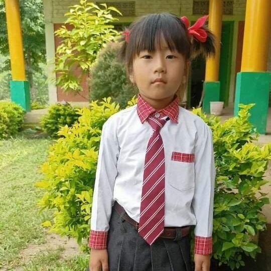 A young girl in school uniform standing outside.