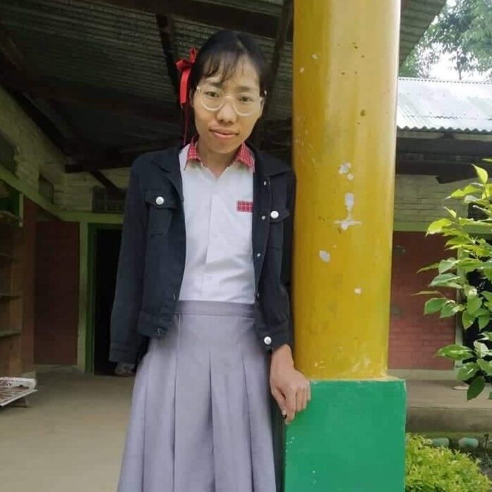 A girl standing next to a pole in front of a building.