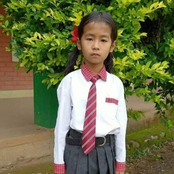 A young girl in school uniform standing next to a tree.