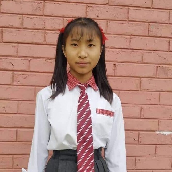 A girl in school uniform standing against a brick wall.